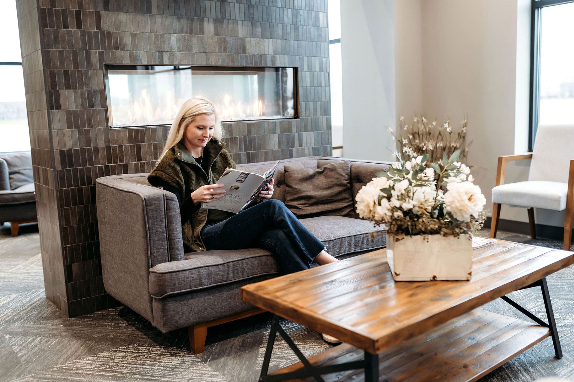 Woman reading in the cozy Village Dental at Saxony lounge with a modern fireplace and floral decor in Fishers, IN
